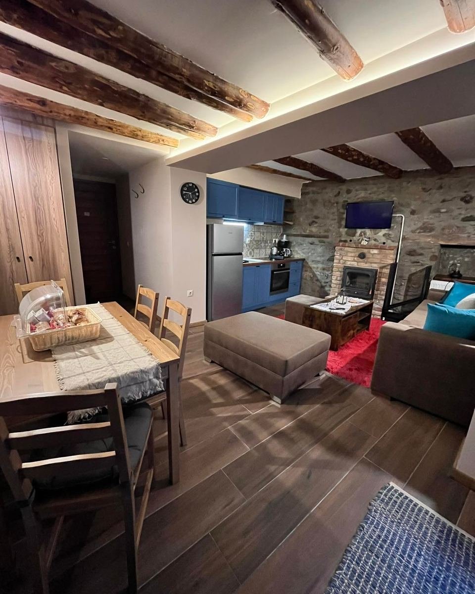 Open-plan kitchen, dining table and living area with a fireplace, under exposed beams.