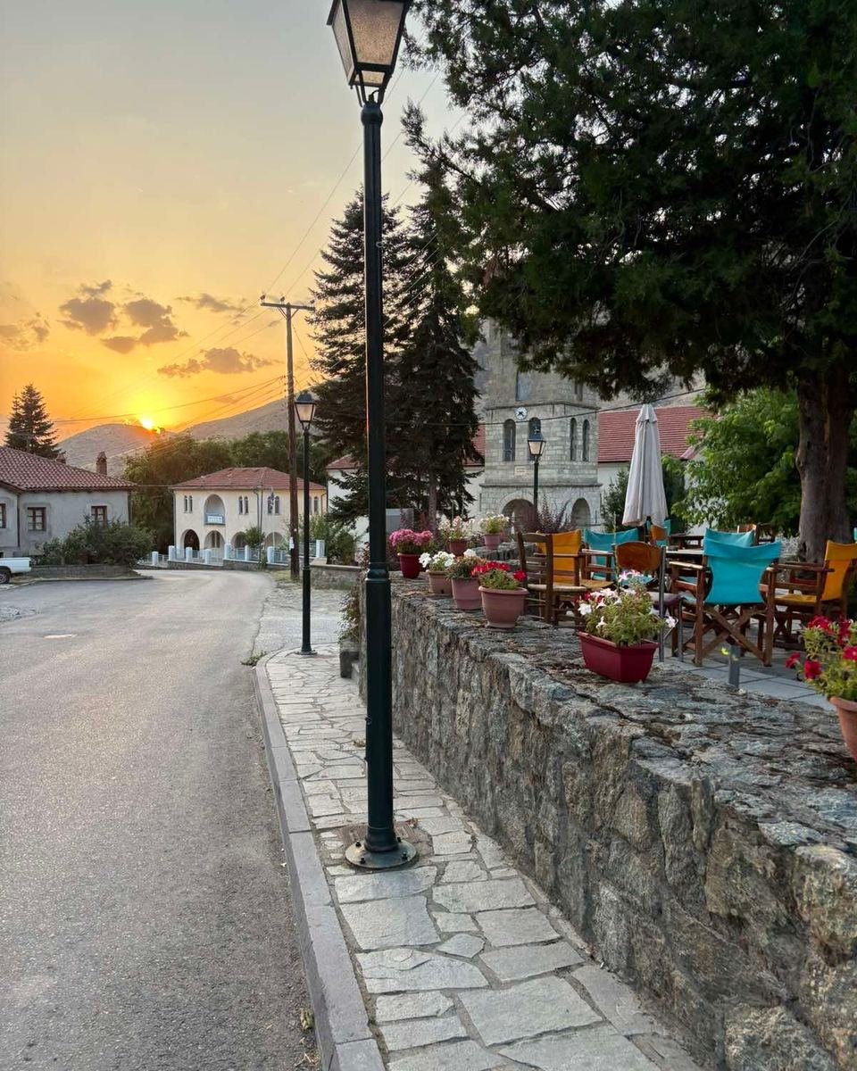 Sunset over a village street with a lamp post and a stone wall.